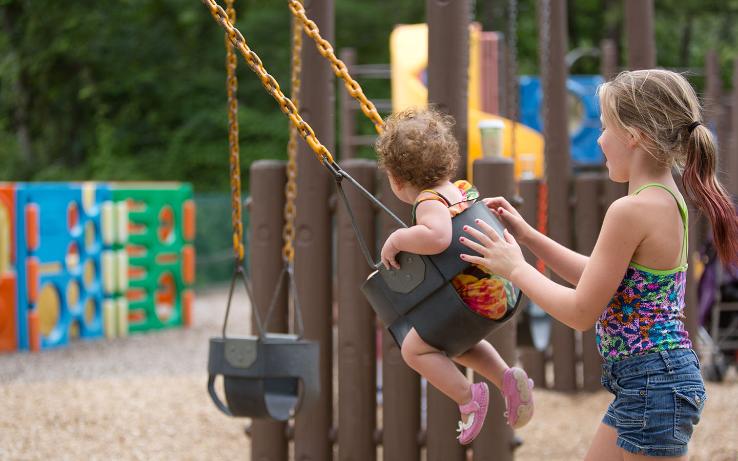 Young woman pushing toddler in a swing.