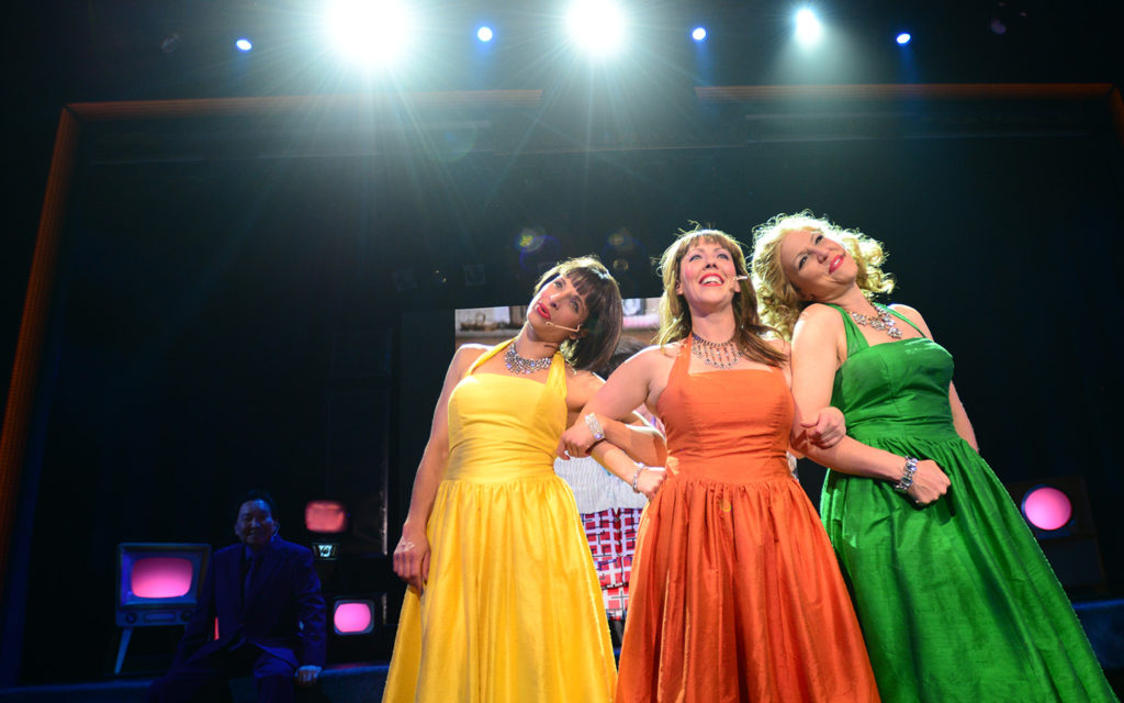 Three women in dresses on stage.