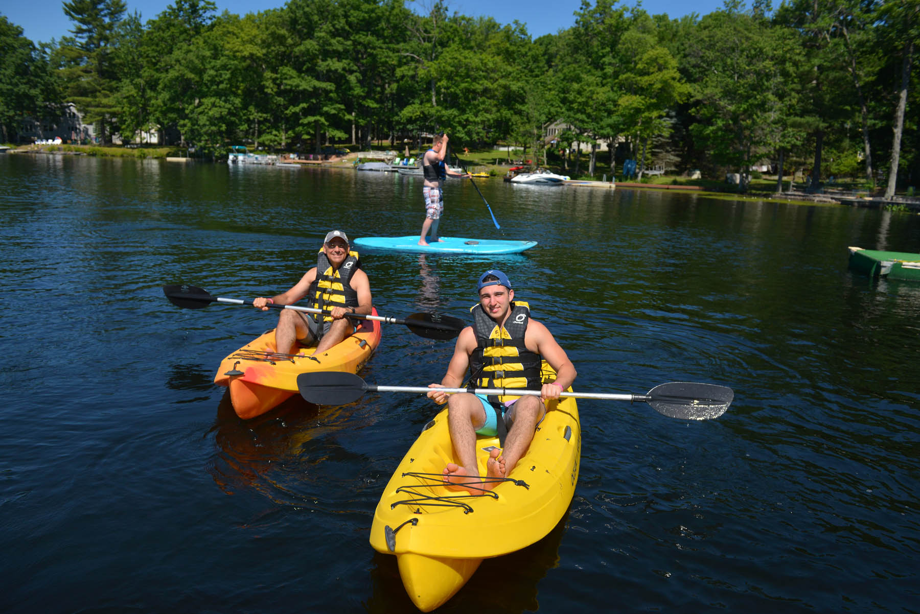 Guests on the lake in kayaks and a standup paddleboard.