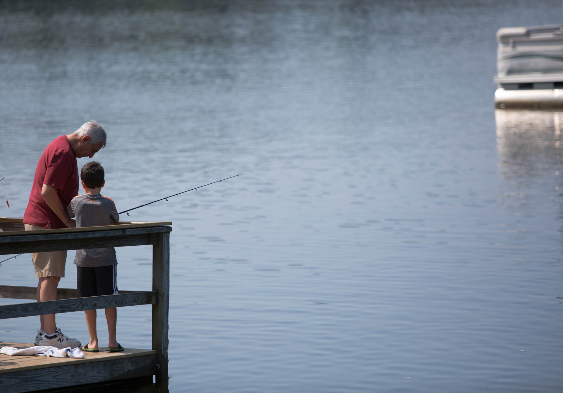 Grandparent and young boy fishing off a pier.
