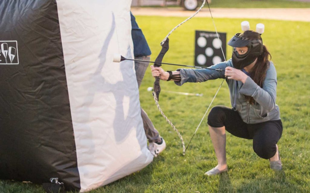 Guest with archery tag bow and arrow behind an inflatable barrier.