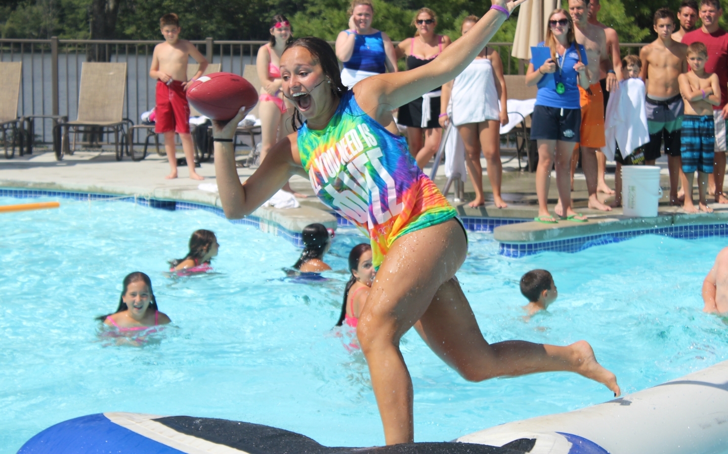 Young woman running on inflatable pool item and throwing a football.