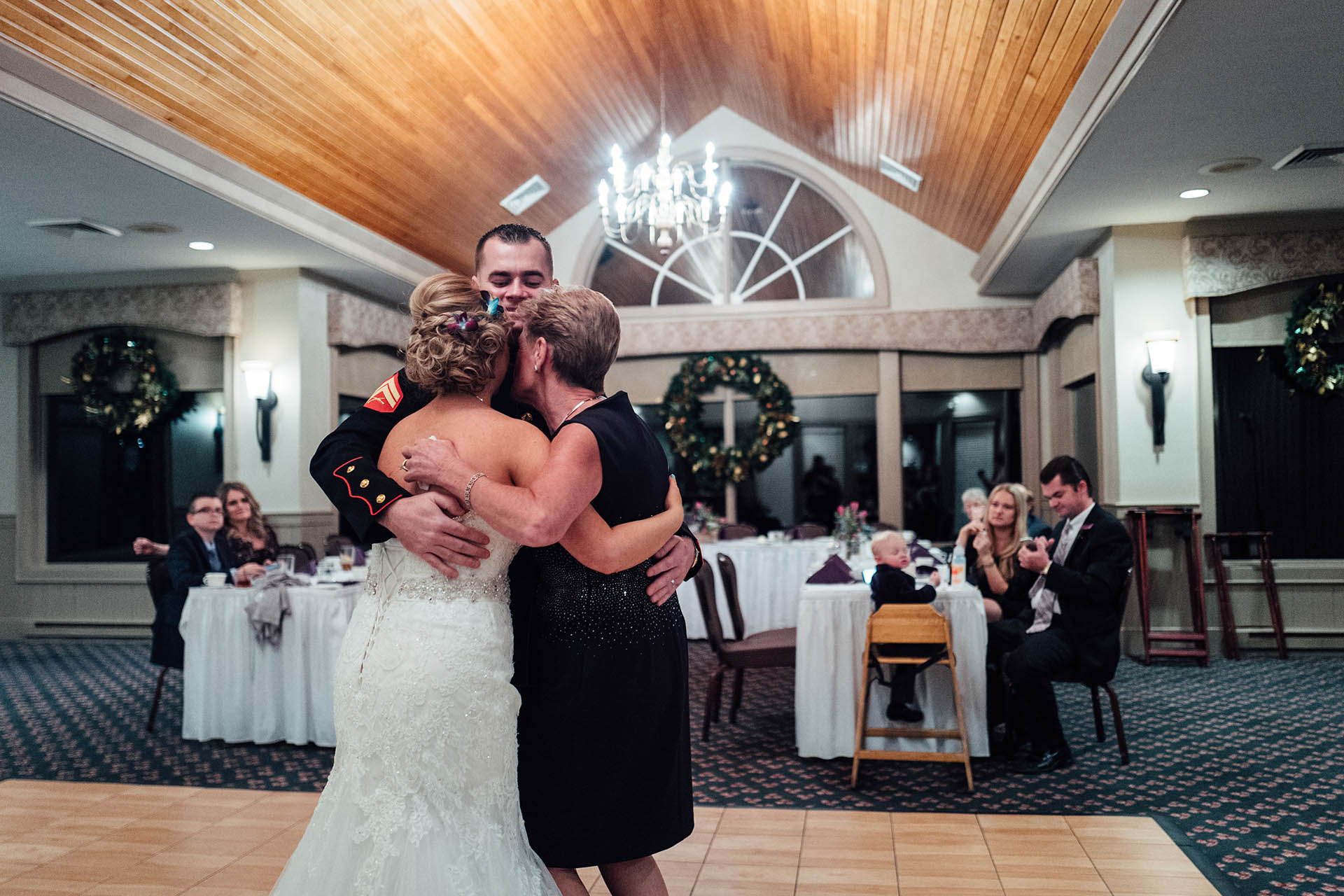 Bride, mom and man in uniform hugging.