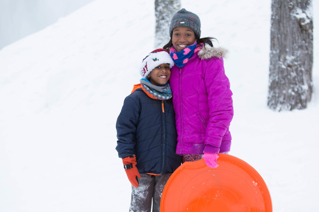 Sister and brother standing in the snow with snow saucer