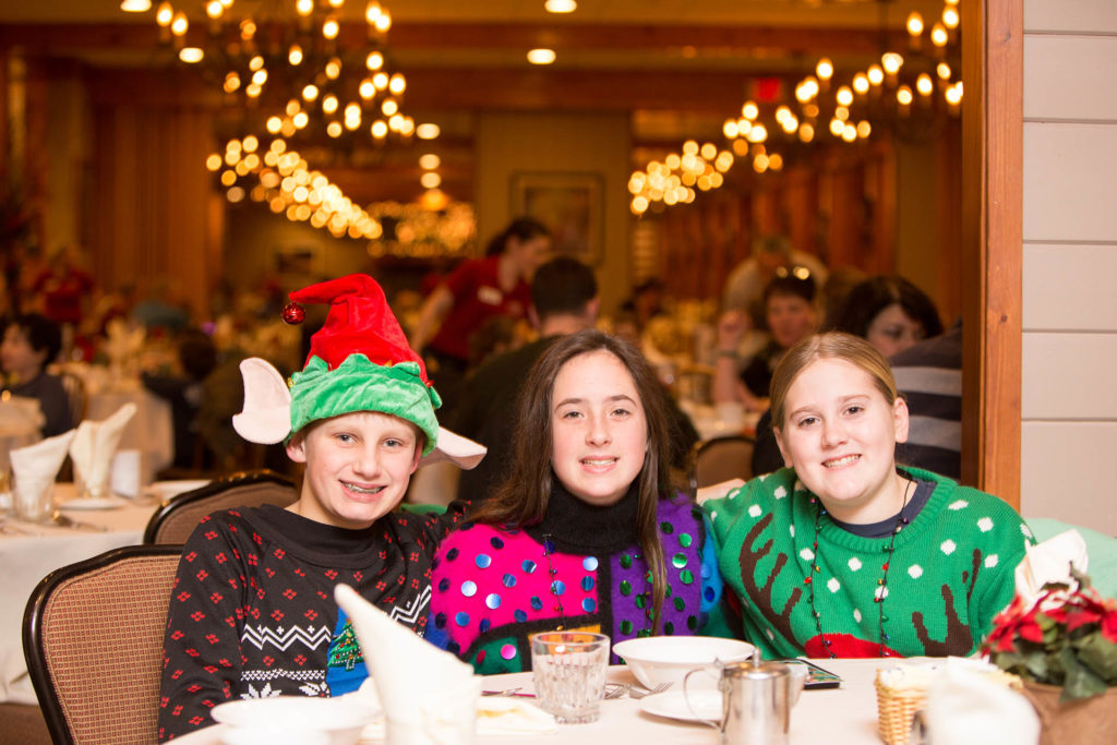 Three young people at a dining table wearing christmas sweaters.