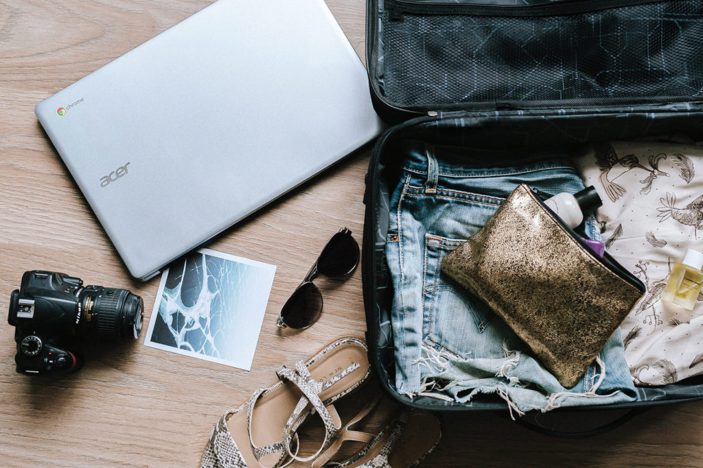 Stock image of open suitcase, laptop, sunglasses, sandals and digital camera.