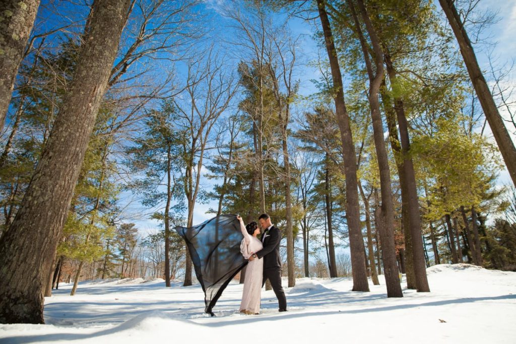 Bride and groom embracing in the woods in winter.