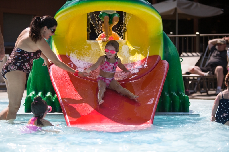 Young girl sliding down a small waterslide in an outdoor splashpad.