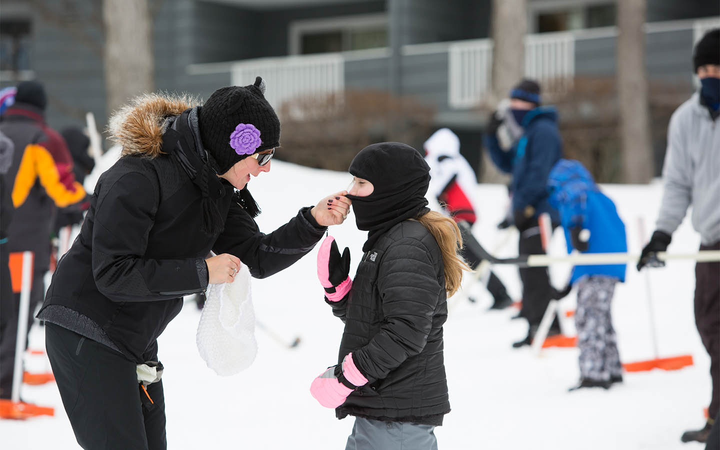 Adult helping woman with her ski mask.