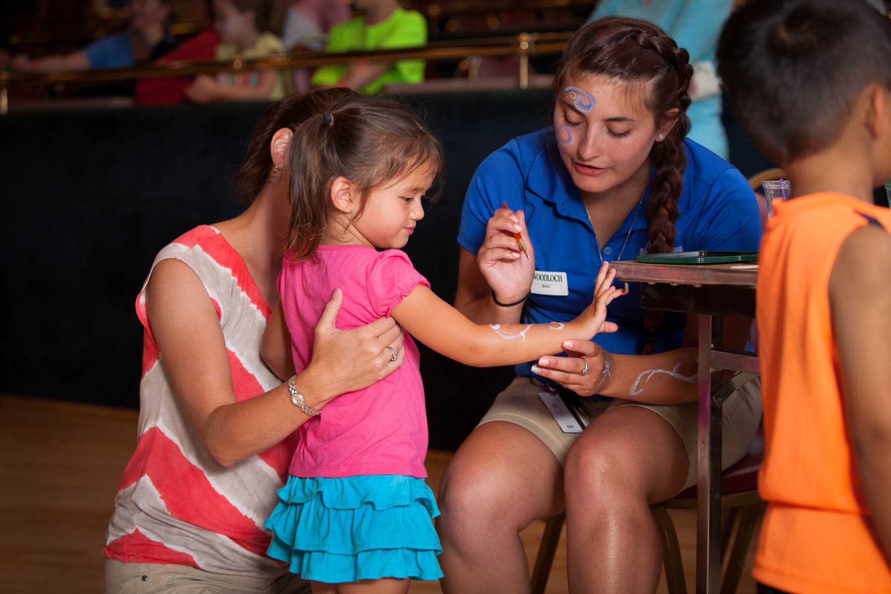 Woodloch employee painting designs on a young girl's arm.