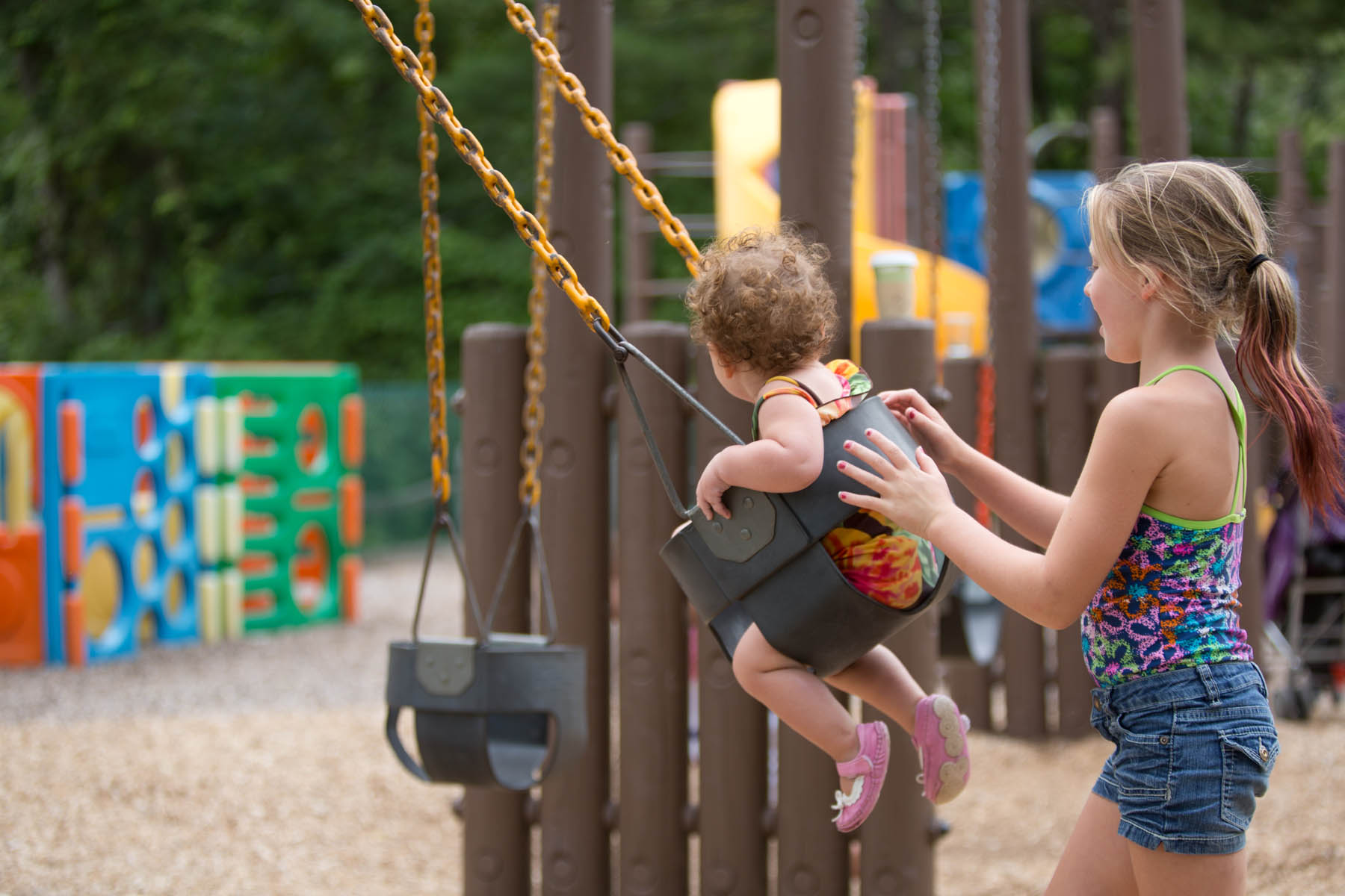 Young woman pushing toddler in a swing.