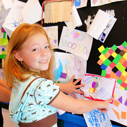 Young girl putting her artwork on a wall with other pictures.