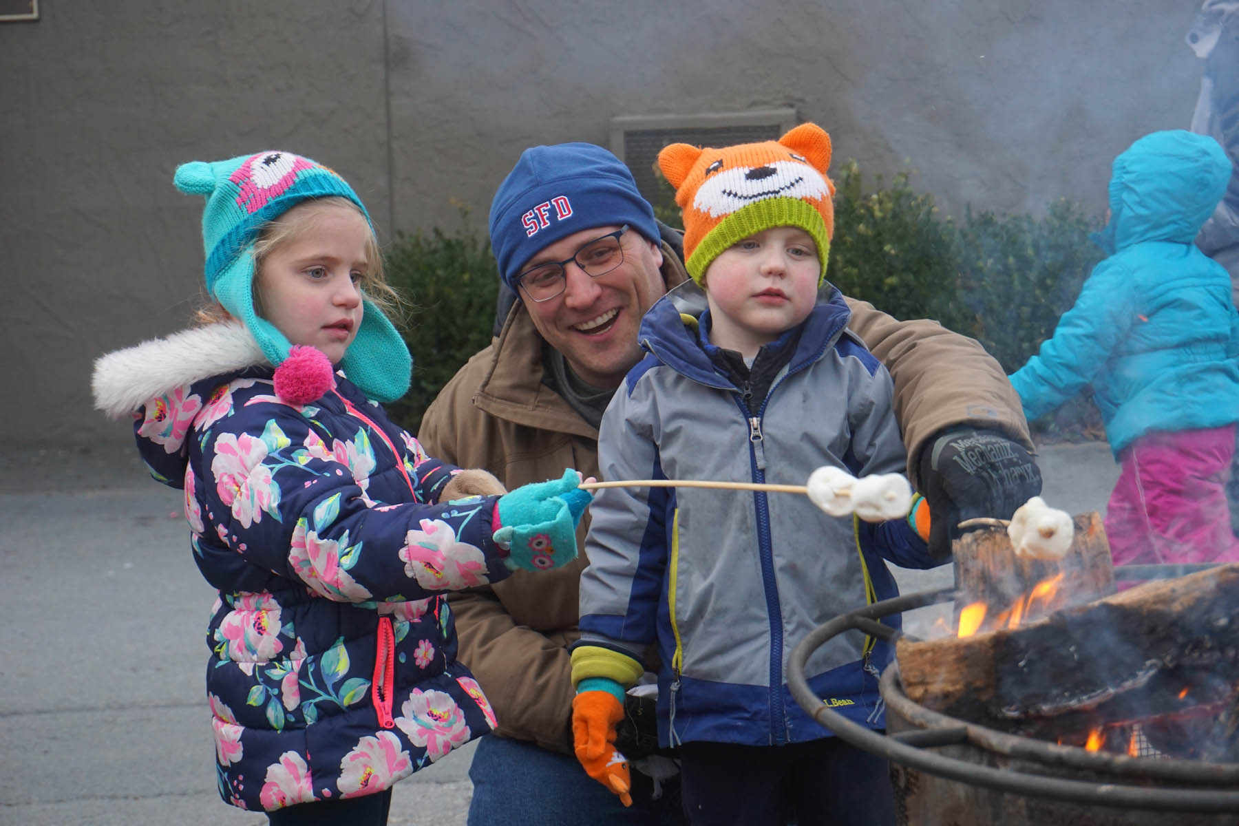 Parent and young kids roasting marshmallows.