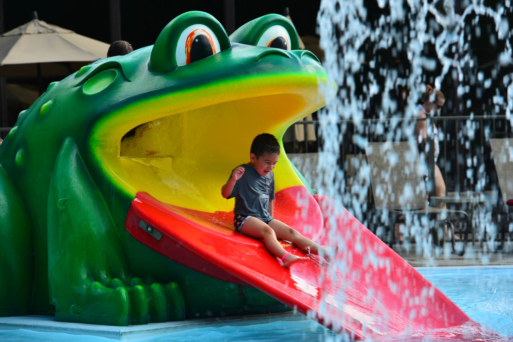 Child sliding down splash pool frog slide.