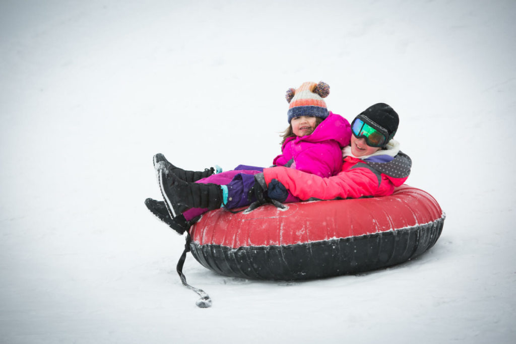 Two young kids sledding downhill in an inner tube.