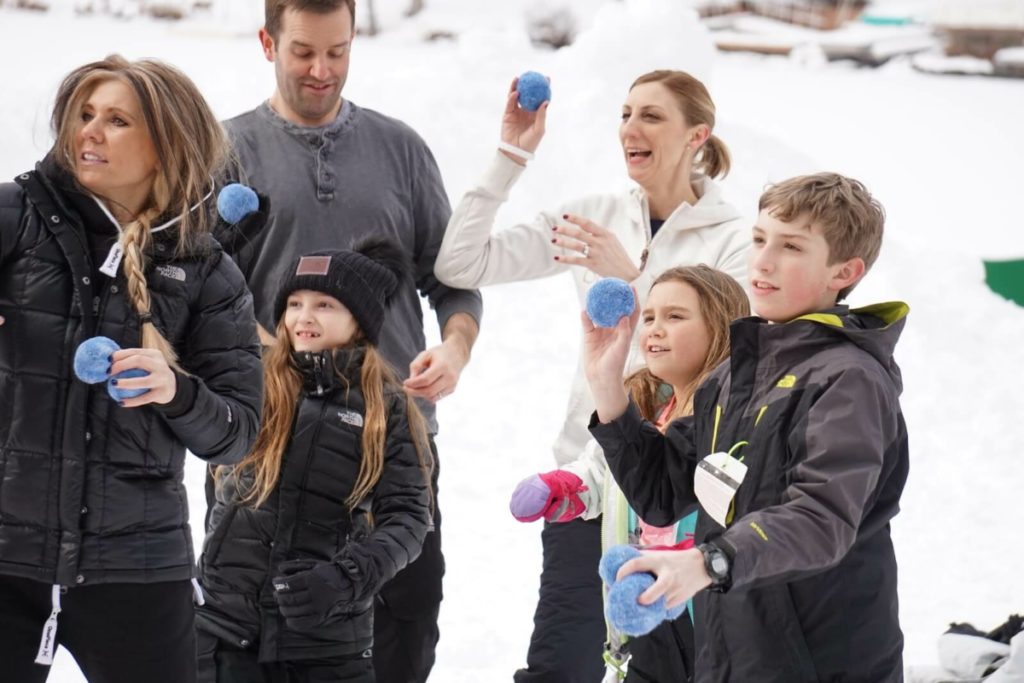 Adults and children throwing blue balls outdoors in winter.