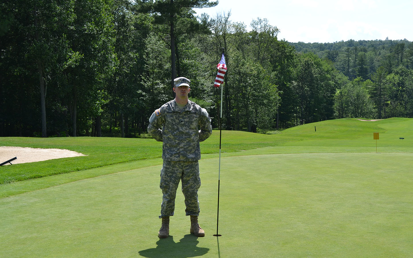 Soldier standing at attention next to a golf hole.