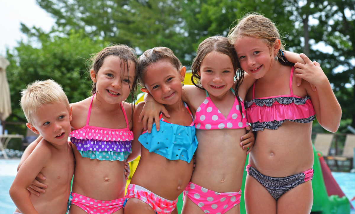 Young girls and boy posing by outdoor pool.