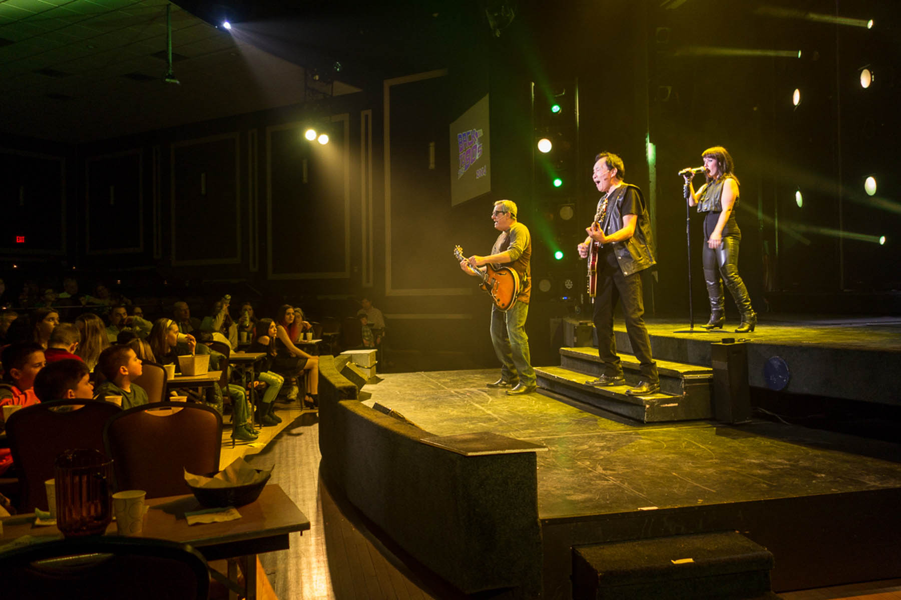 Two men and woman performing rock music on stage.