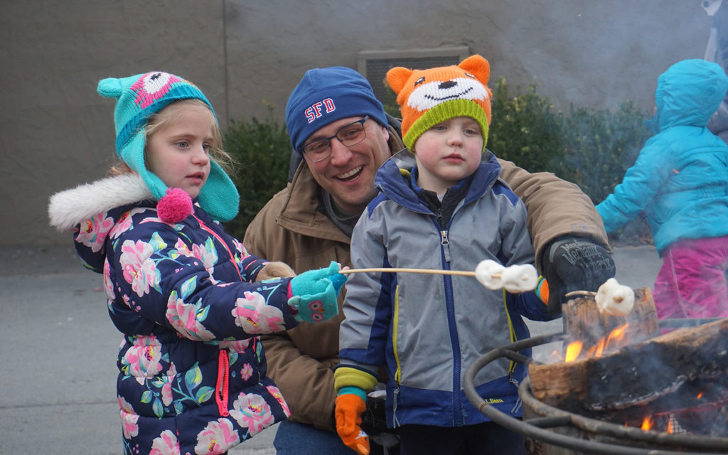 Man with a young boy and girl roasting marshmallows.