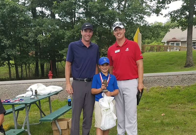 Adult golf coaches with junior golfer holding medals and trophy.