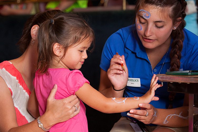 Woodloch employee painting spirals on young girls arm.