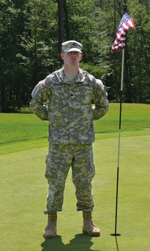 Army personell standing at attention next to golf hole with American flag.