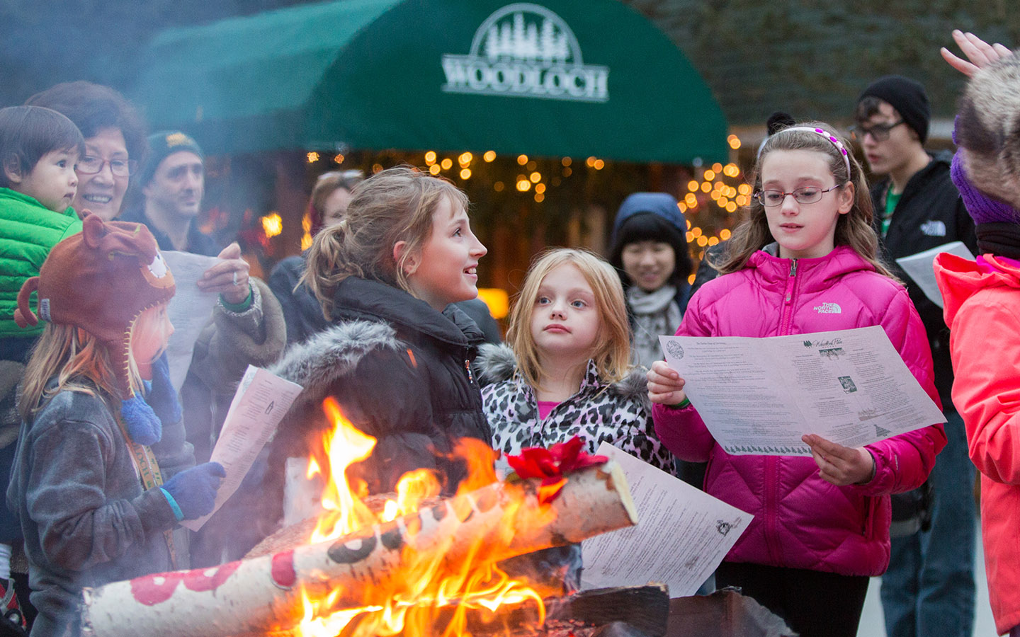Young people reading menus outdoors next to Yule log fire.
