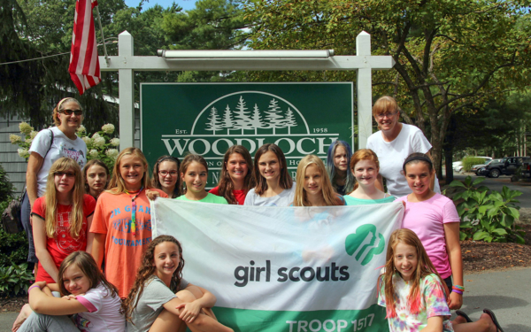Girl Scouts posing with their Troop flag and Woodloch sign.