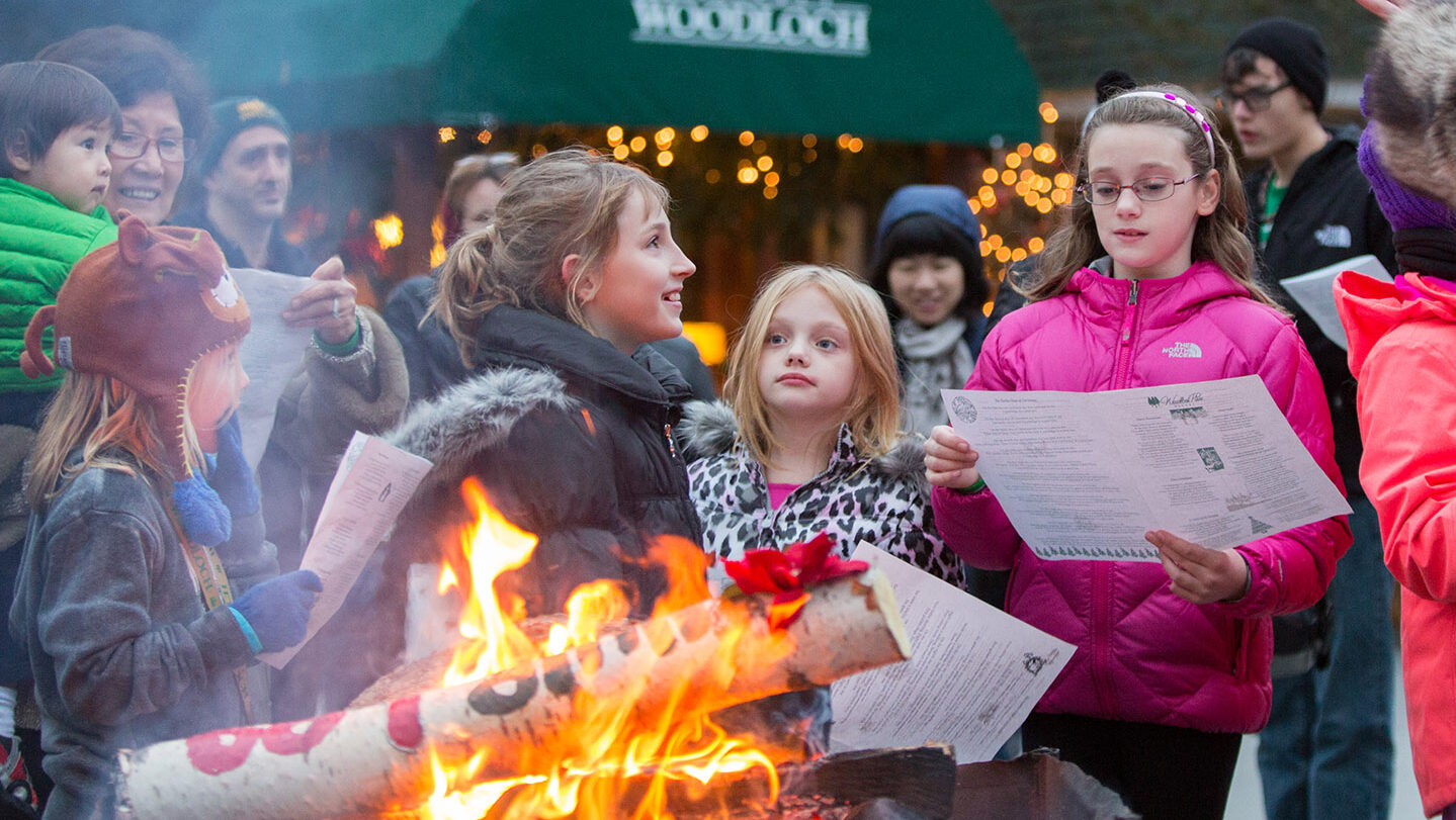 Young people reading menus outdoors next to Yule log fire.