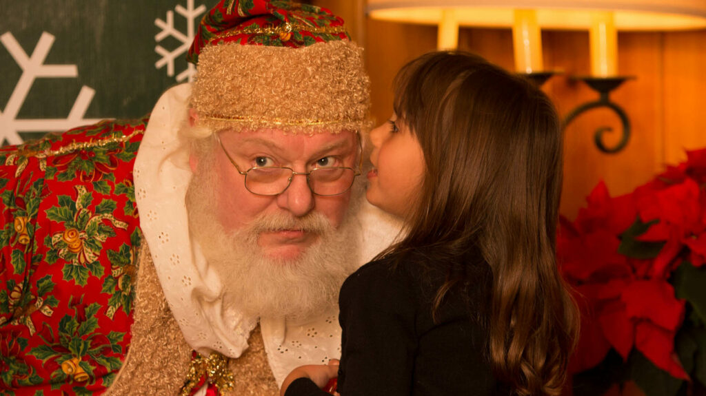 Young girl whispering into Santa's ear.