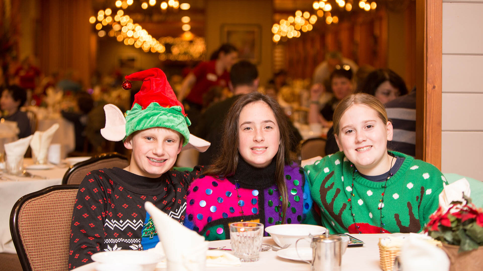 Three young people at a dining table wearing christmas sweaters.