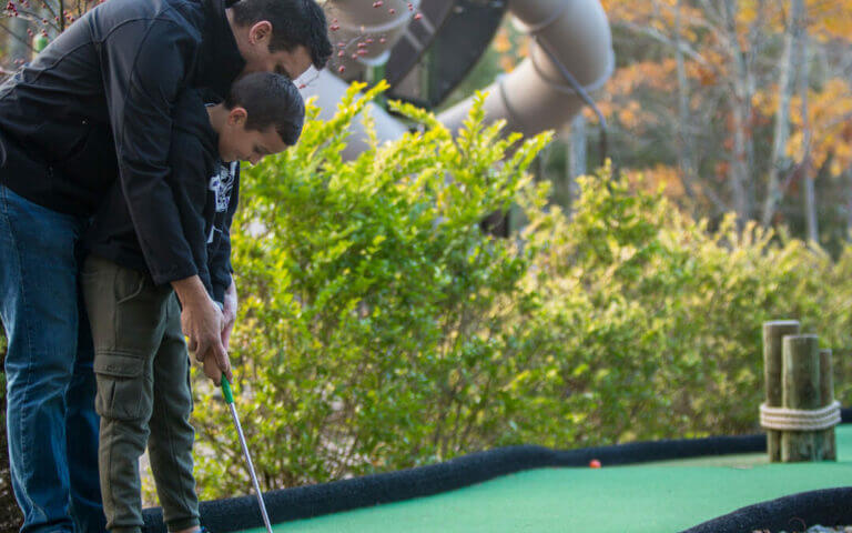 A father and son playing mini golf on a Poconos spring break vacation at an all-inclusive resort.