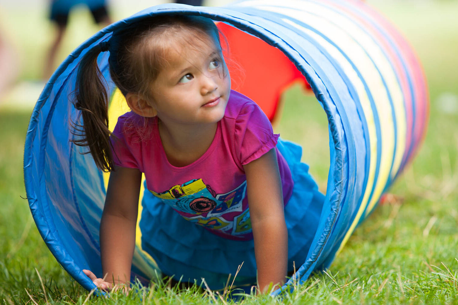 Young girl crawling through a pop-up play tunnel.