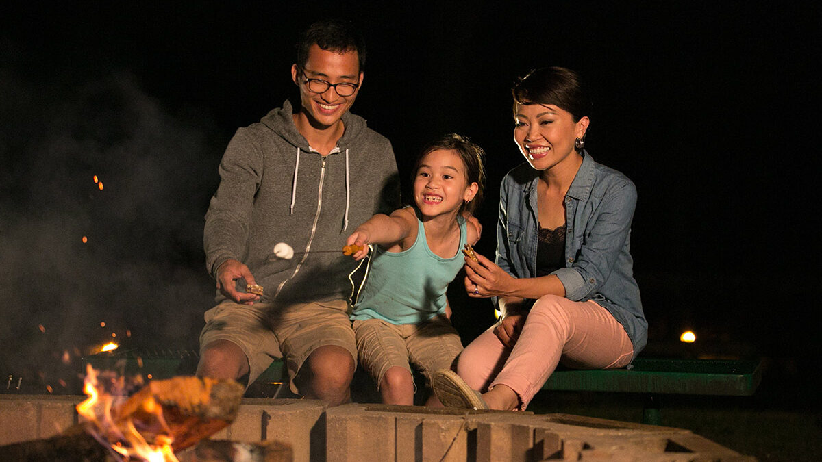 Parents and daughter roasting marshmallows at campfire
