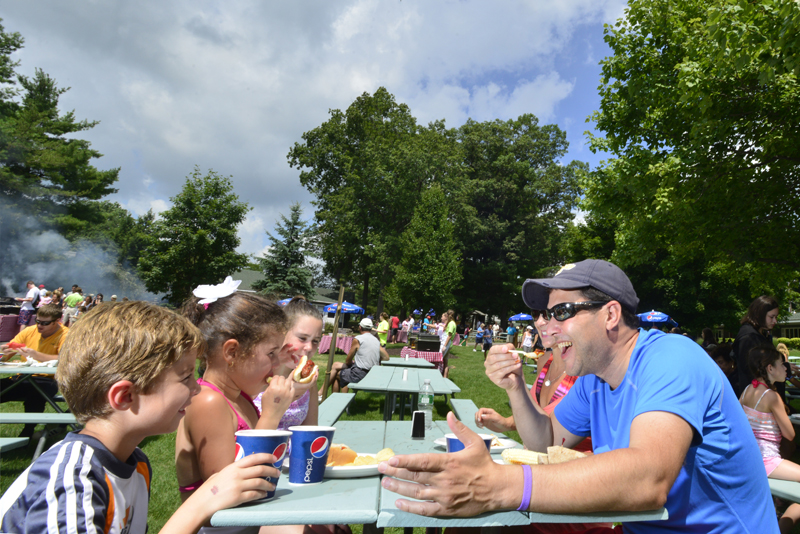 Adults and kids at picnic table eating hotdogs and burgers.