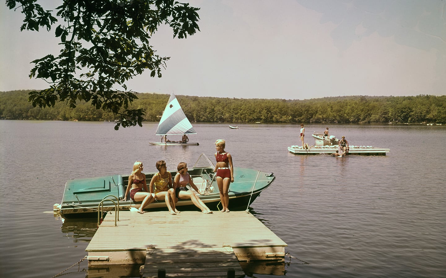 Historic photo of four people in swimsuits on boat and floating dock.