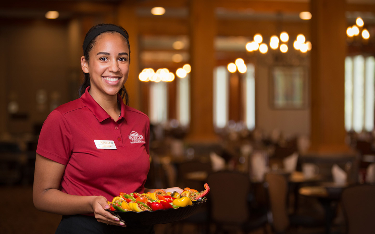 Server in dining room with plate of food.